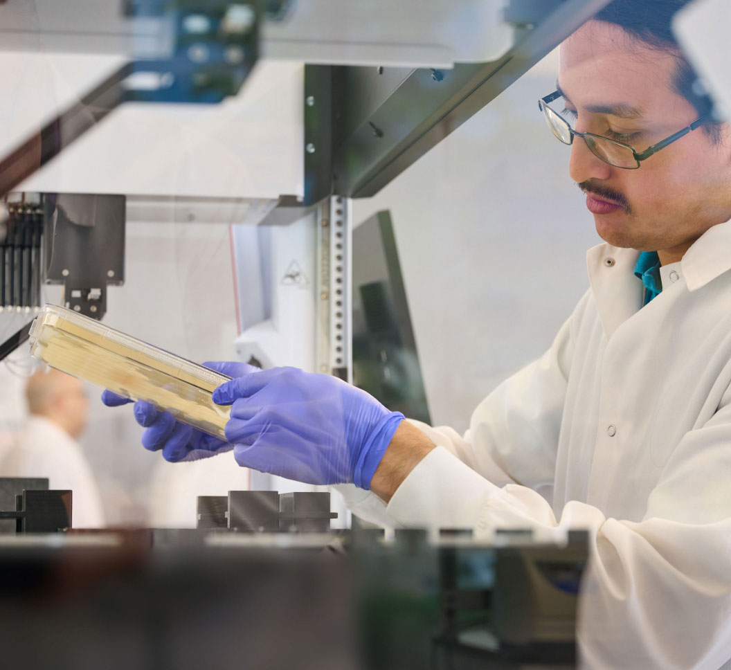 A person in a lab coat and gloves looking at a bacterial plate in a laboratory