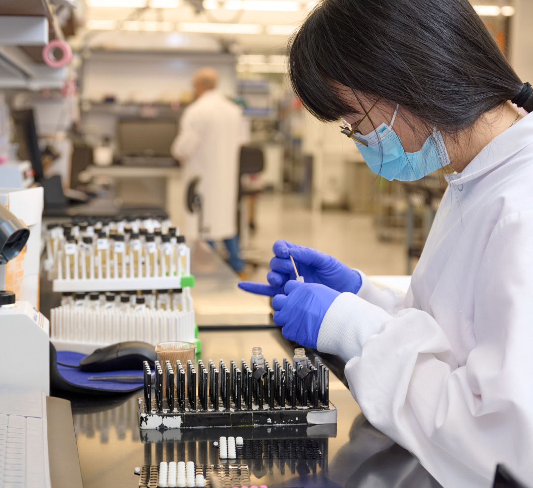 A person wearing a lab coat and gloves putting a toothpick in a vial