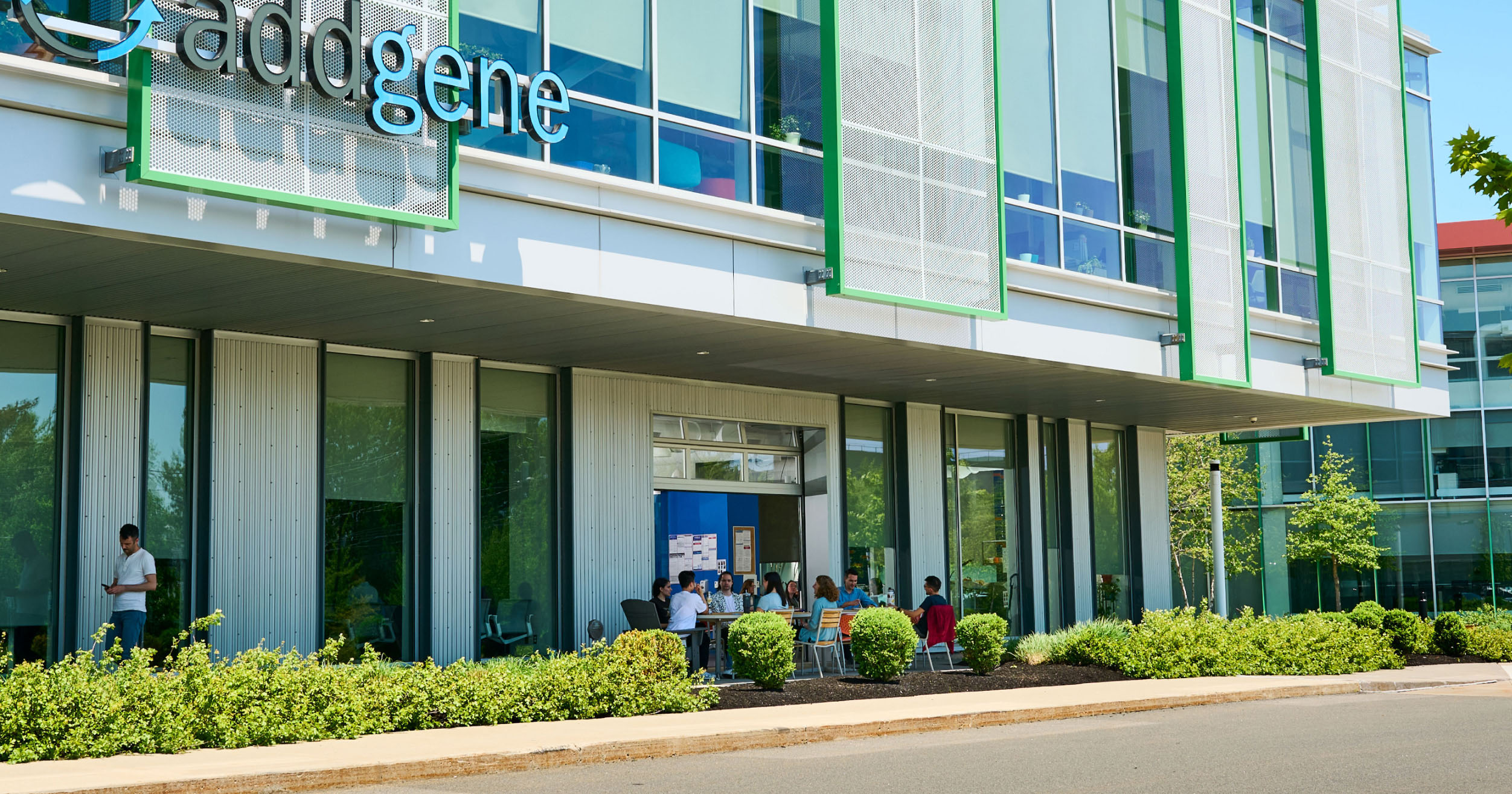 A building with glass windows and an Addgene sign. People sitting outside on a sunny day.